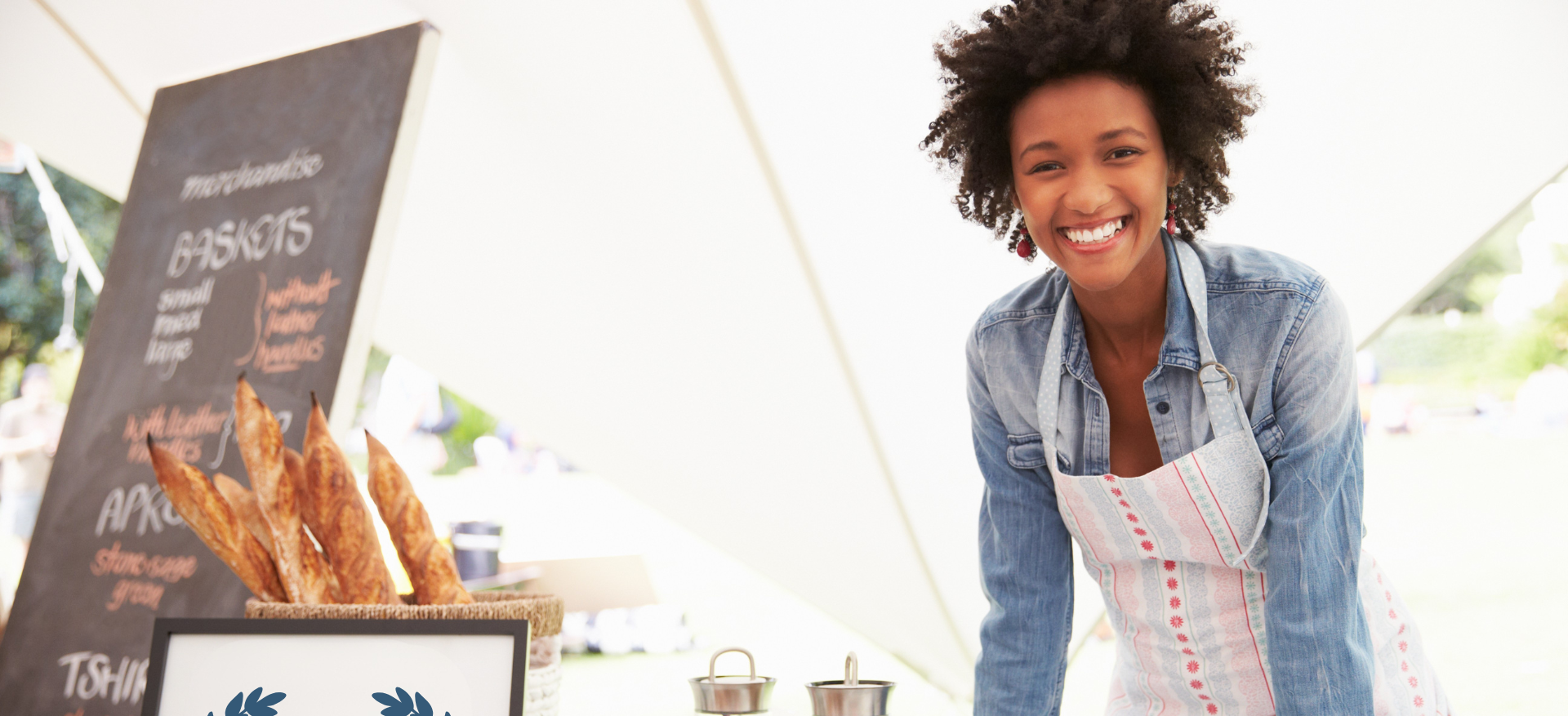 Woman working at a farmers market stand inside tent with fresh bread
